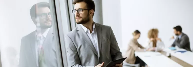 Businessman in a suit with a tablet, looking out of a window.