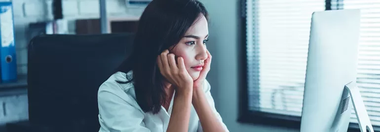 A woman in a white shirt staring intently at a computer screen in an office setting.