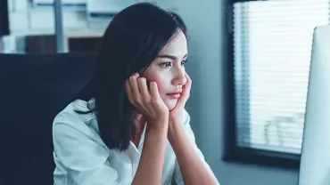 A woman in a white shirt staring intently at a computer screen in an office setting.