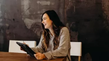 Woman smiling while holding a tablet at a wooden table