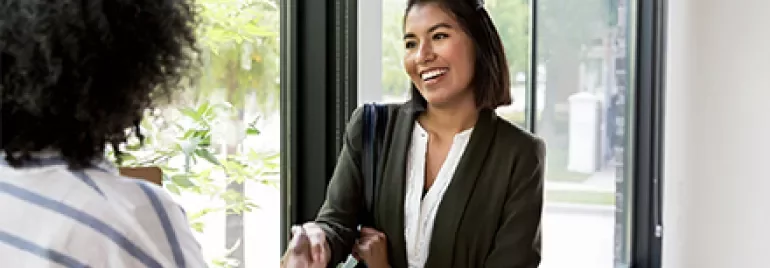 Two women shaking hands by a sunlit window.