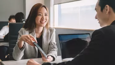 Two professionals talking at a table in an office setting.