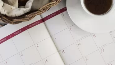 Open calendar with a basket and coffee cup on a white table.
