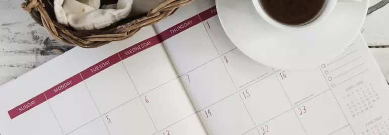Open calendar with a basket and coffee cup on a white table.