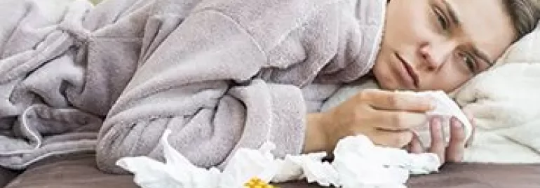 Person in a robe lying on a couch surrounded by tissues and medication.