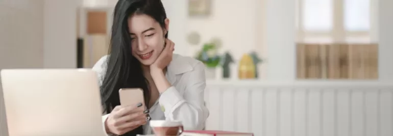 Woman smiling at phone in a cozy cafe with a laptop and coffee.
