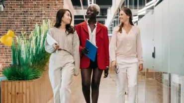 Three professionals walking in a modern office corridor with brick and glass walls.