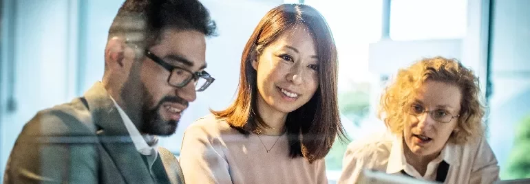 Three people working together at a desk, focused on a computer screen.