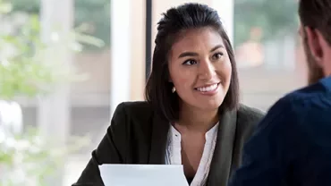 Woman smiling during a meeting with a man, seated at a table with documents.