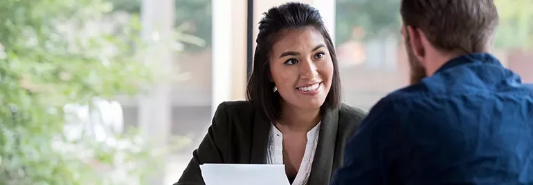 Woman smiling during a meeting with a man, seated at a table with documents.