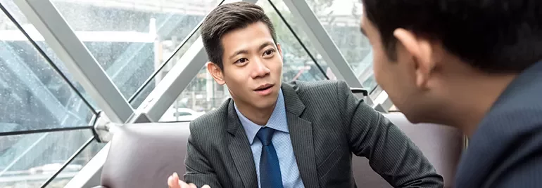 Two colleagues in suits having a discussion in a modern office setting.