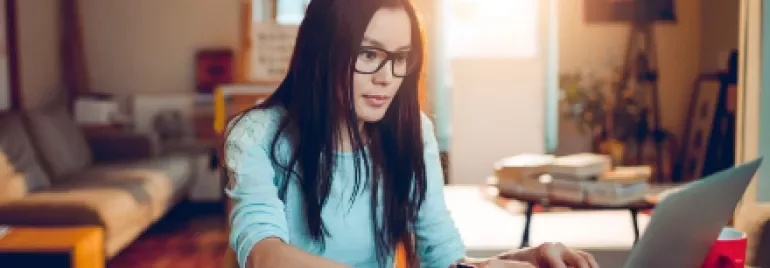 Woman with glasses working on a laptop in a cozy living room.